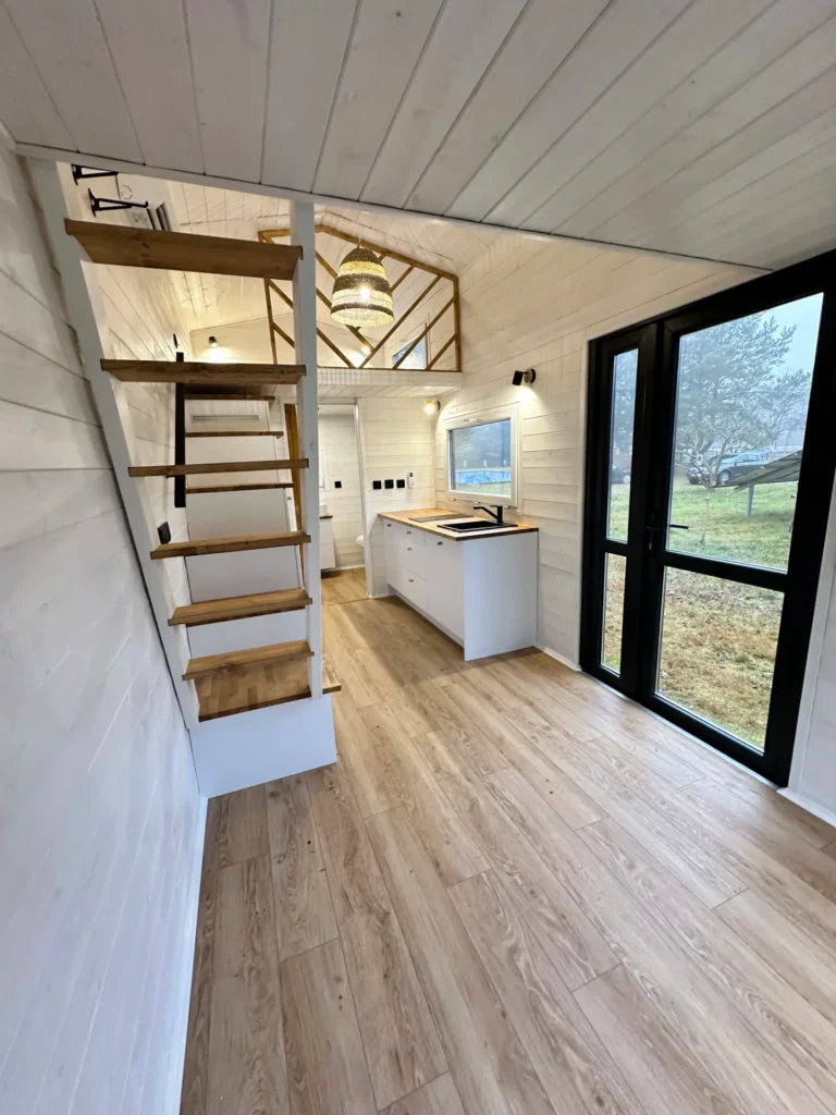 Nowoczesne wnętrze mobilnego domku z drewnianymi schodami, kuchnią, dużymi oknami i przestronnym salonem.