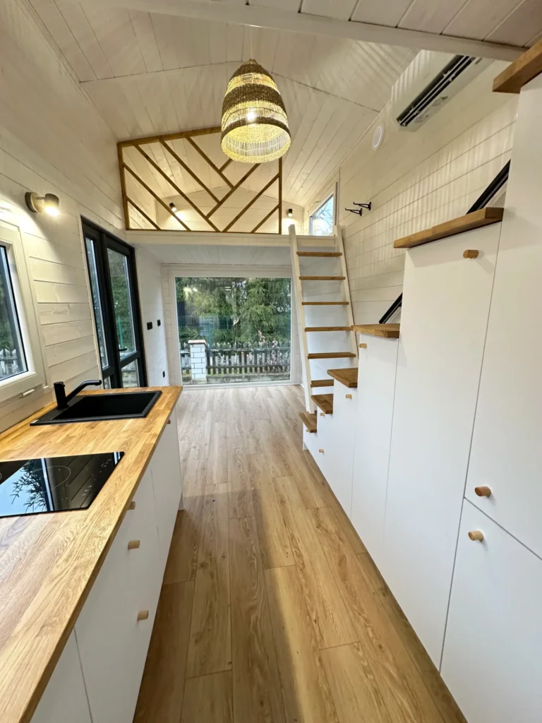 Nowoczesne wnętrze mobilnego domku z kuchnią, drewnianymi schodami, przestronnym sufitem i dużymi oknami.