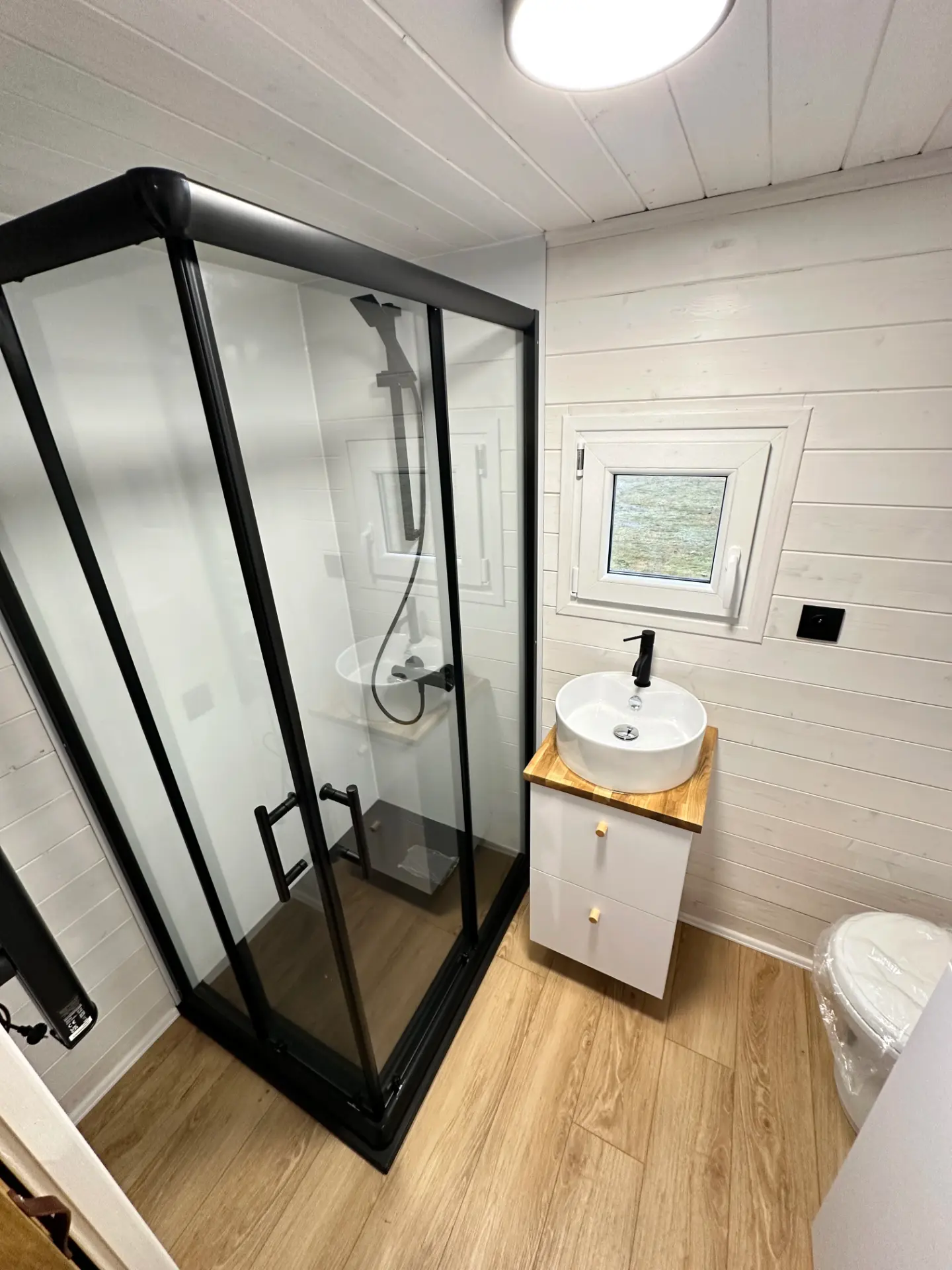 Nowoczesna łazienka w mobilnym domku z prysznicem, umywalką i toaletą, drewnianą podłogą.