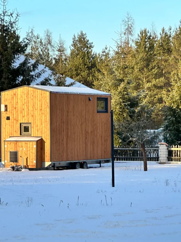 Mobilny domek z drewnianą elewacją, zaśnieżony teren, las iglasty w tle.